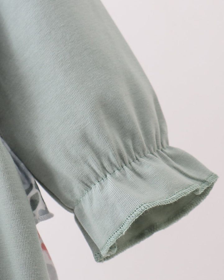 Close-up of a sage green fabric sleeve with a gathered elastic cuff, showing the texture and stitching against a light background.