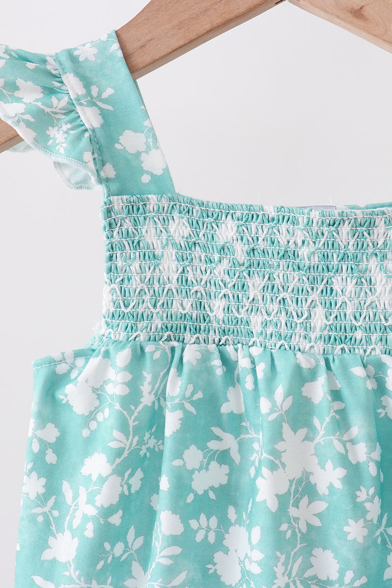 Teal dress with white floral pattern on a wooden hanger against a white background