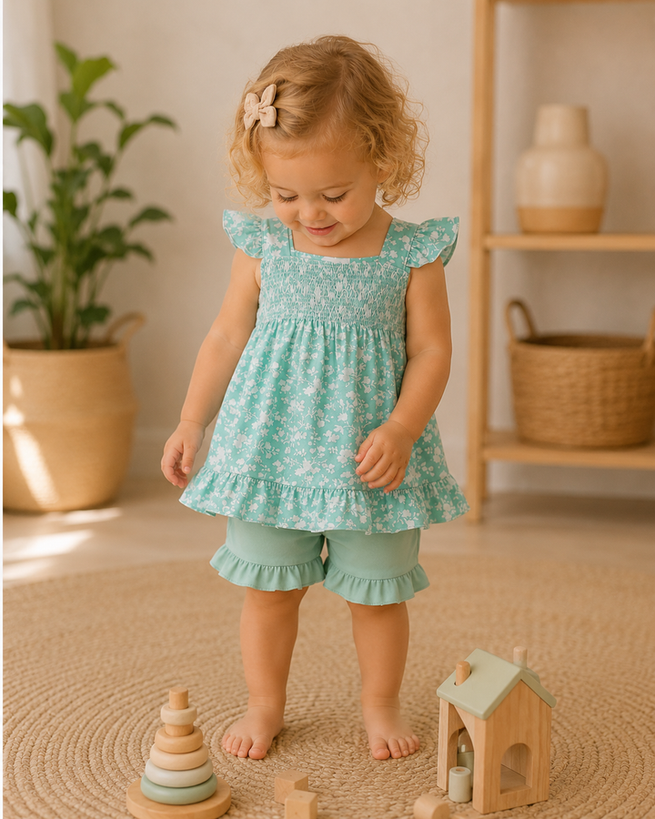 Young child in a light blue floral dress and shorts standing on a beige rug with wooden toys.