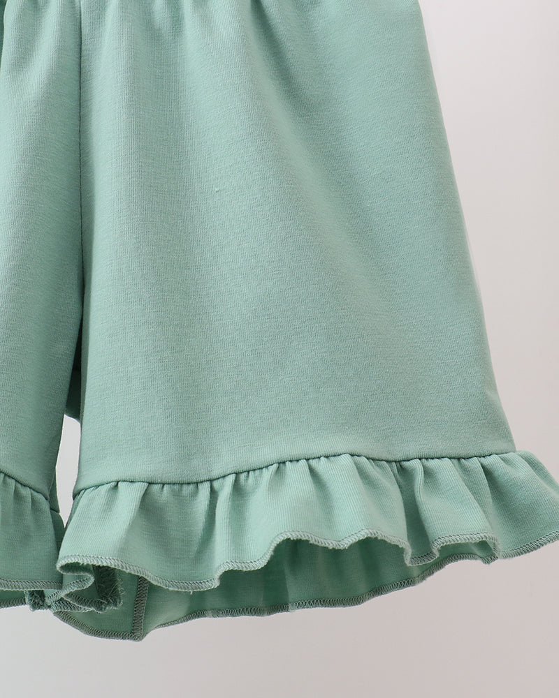 Green shorts with ruffled hem on a light gray background