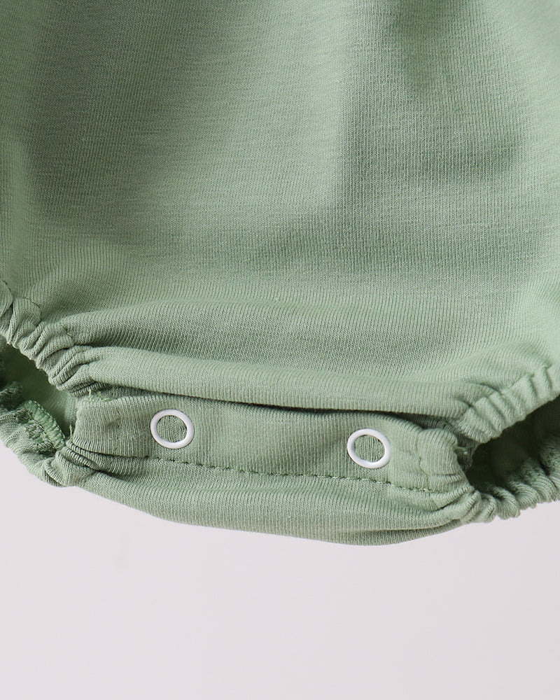 Close-up of a green baby romper with buttons on a light gray background