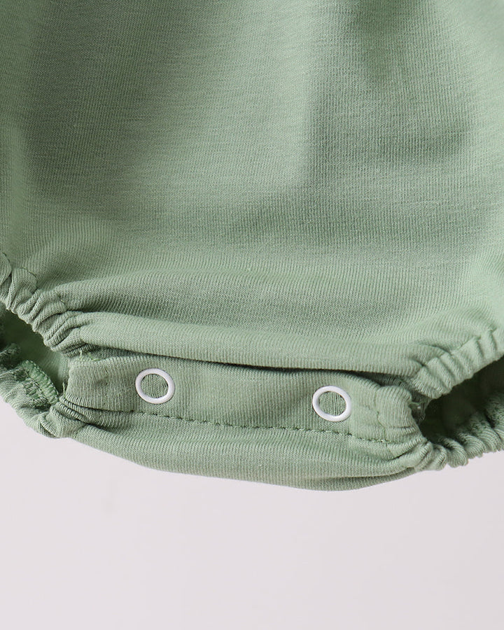 Close-up of a green baby romper with buttons on a light gray background