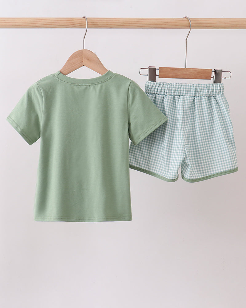 Green t-shirt and checkered shorts on hangers against a light gray background