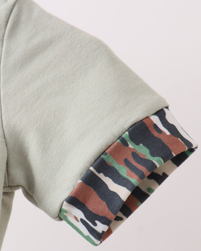 Close-up of a light sage green sleeve with a rolled cuff revealing a multicolor camouflage lining in green, brown, black, and white.