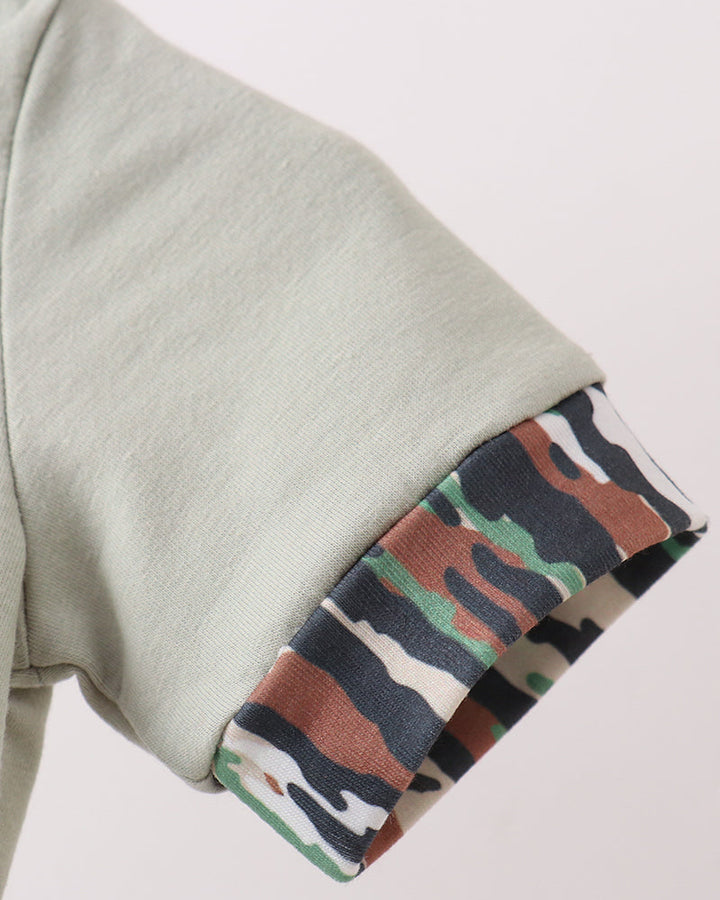 Close-up of a light sage green sleeve with a rolled cuff revealing a multicolor camouflage lining in green, brown, black, and white.