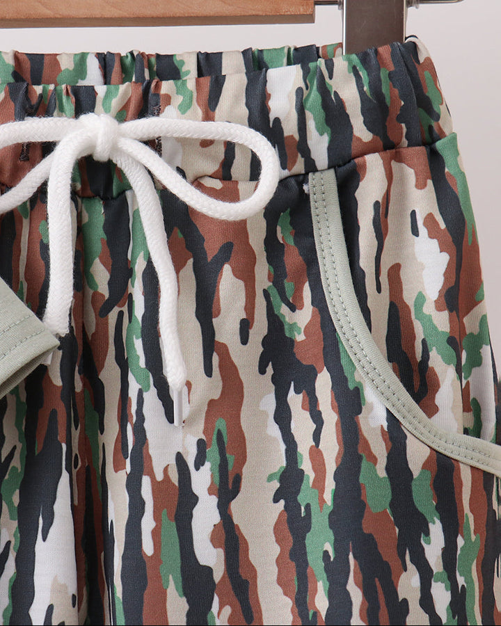 Close-up of camouflage-print pants hanging on a wooden hanger, with a white drawstring and pale green piping details visible.