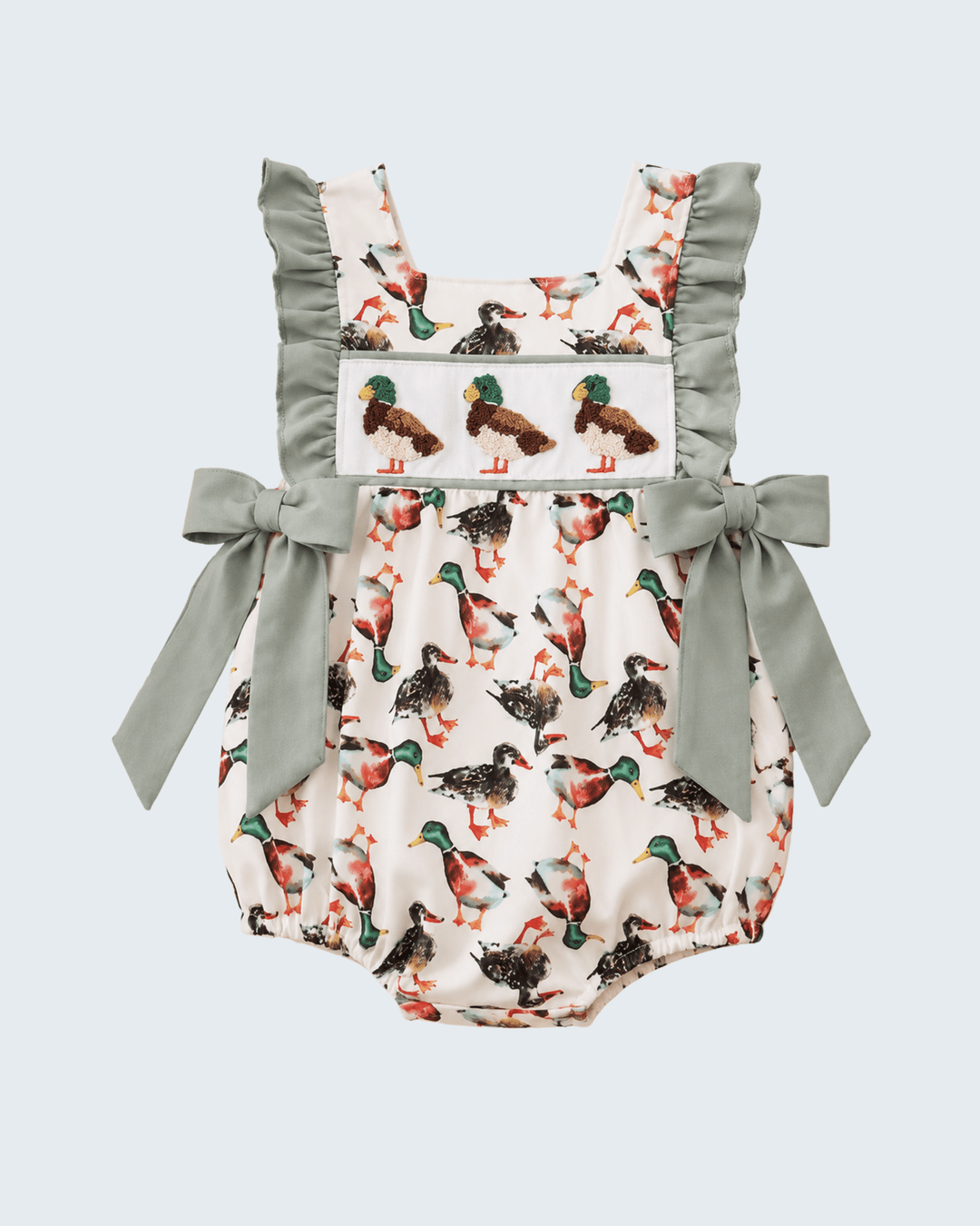 A baby romper with a white background and an all-over duck print, featuring sage green ruffled shoulder straps, matching side bows, and a decorative chest panel with embroidered ducks.