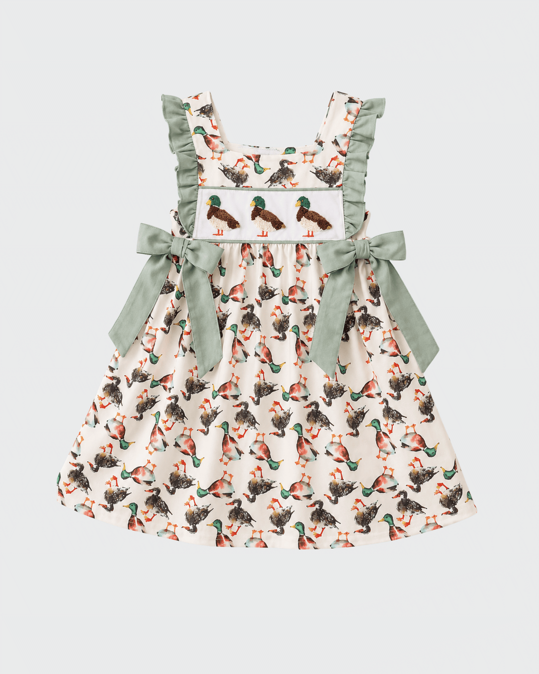 A sleeveless dress with a white base, an all-over duck print, and sage green ruffled shoulder straps and bow details on the sides.