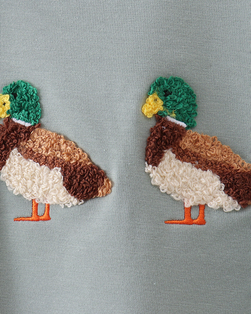 Sage green T-shirt closeup with two embroidered bird patches