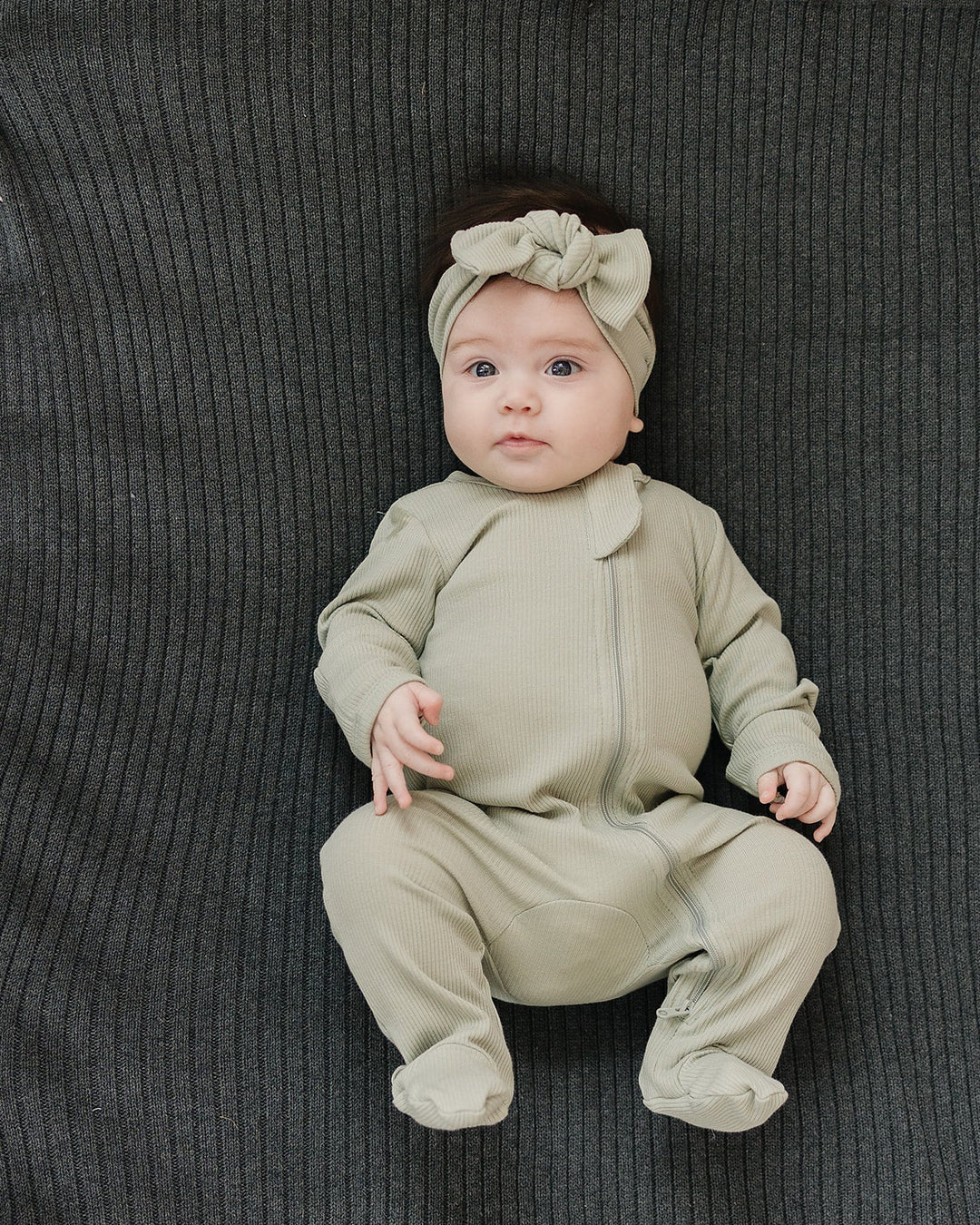 Sage green zip-front footed romper with long sleeves and snaps on baby