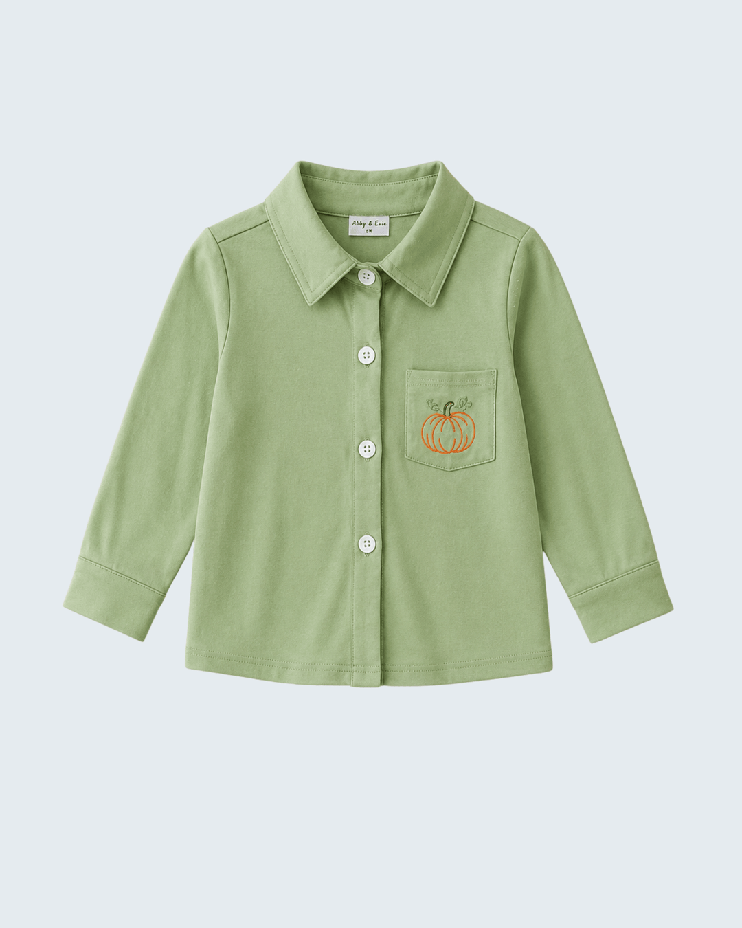 A light sage green long-sleeve button-up shirt for toddlers, featuring a pointed collar, a chest pocket with a small embroidered orange pumpkin, and white buttons, shown against a light gray background.