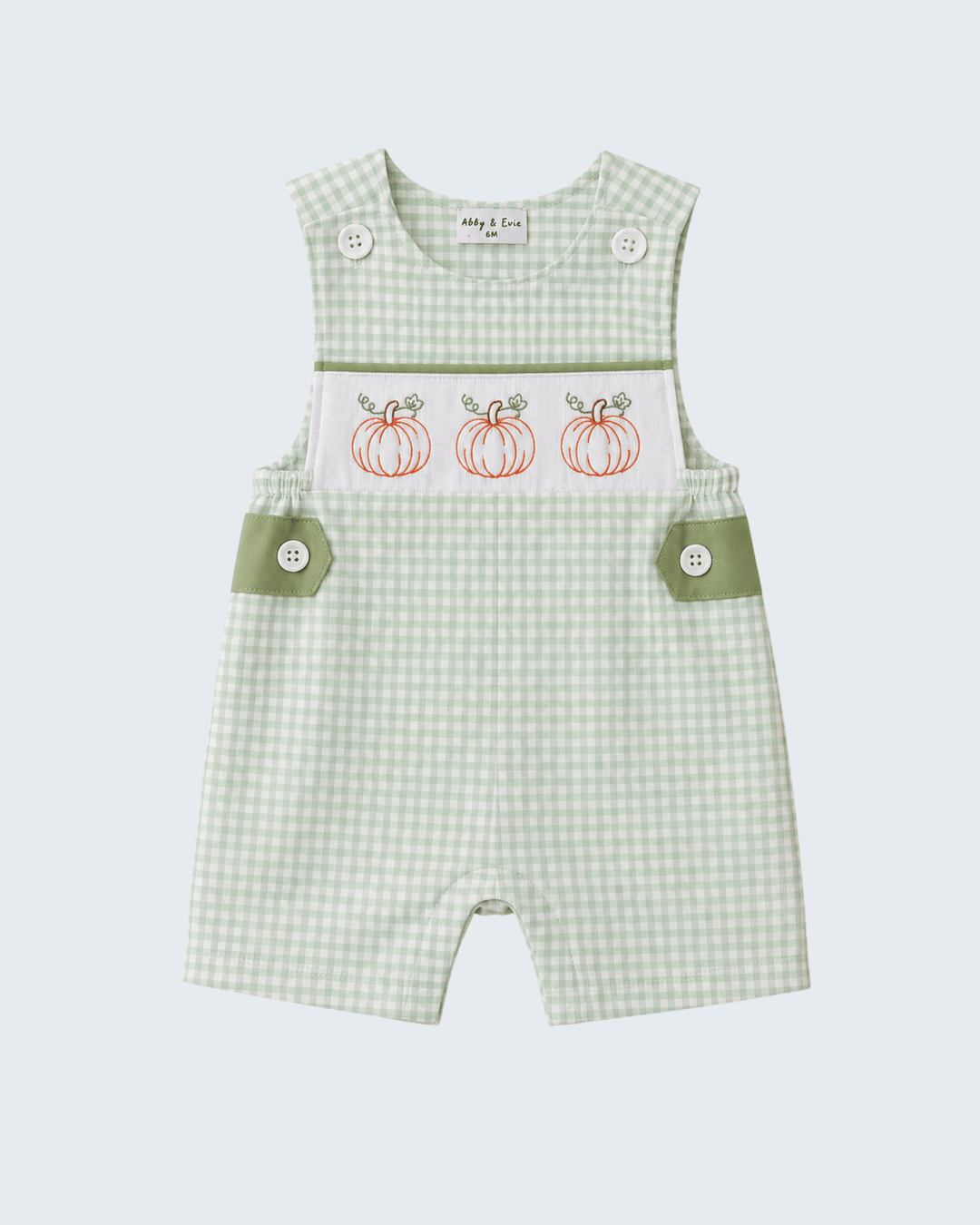 A baby romper in a light green and white gingham pattern, featuring a white chest panel with three embroidered orange pumpkins and sage green side pocket flaps with snap buttons.