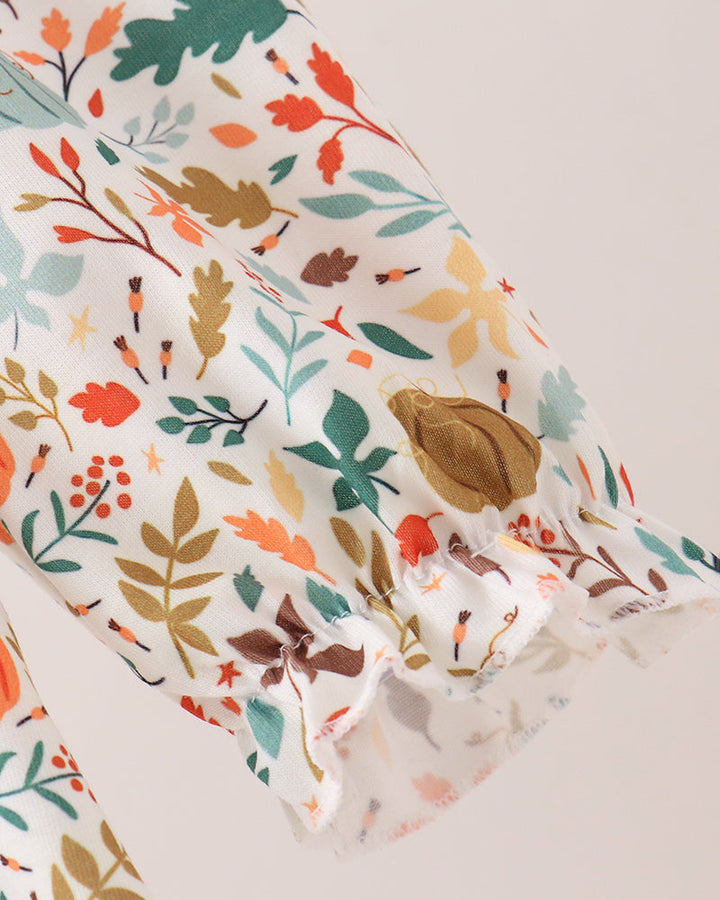 A close-up of a white fabric sleeve or garment section featuring a colorful autumn leaf and berry print in orange, green, brown, and beige, with a ruffled edge.