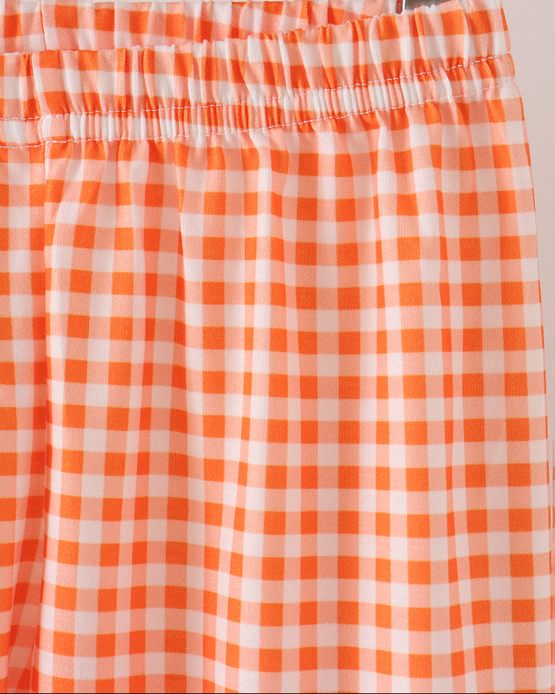 Close-up of an orange and white gingham check pant with an elastic waistband, hanging on a wooden hanger.