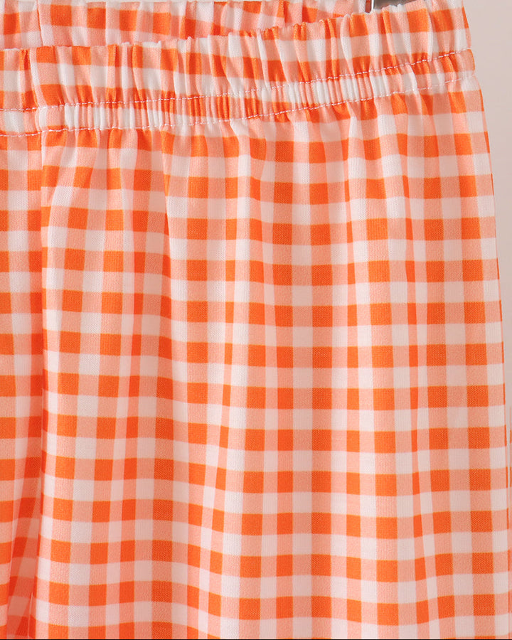 Close-up of an orange and white gingham check pant with an elastic waistband, hanging on a wooden hanger.