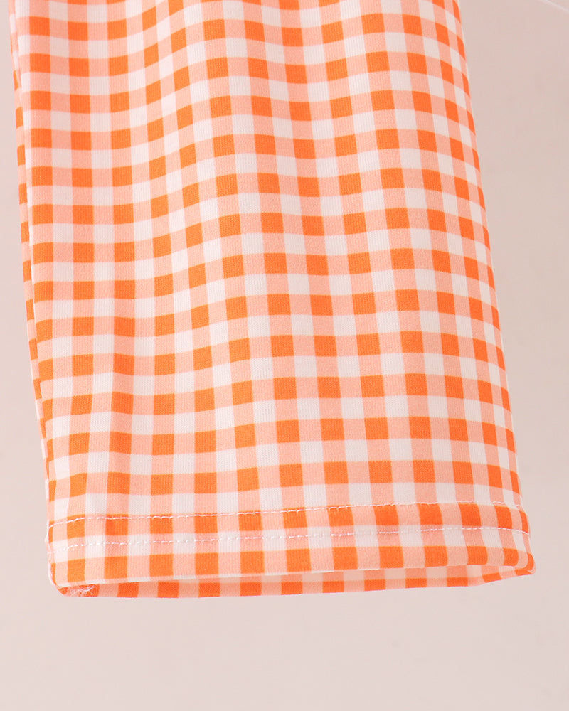 A close-up of a folded fabric item featuring an orange and white gingham checkered pattern, set against a plain light beige background.
