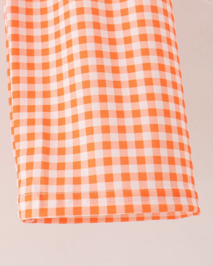 A close-up of a folded fabric item featuring an orange and white gingham checkered pattern, set against a plain light beige background.