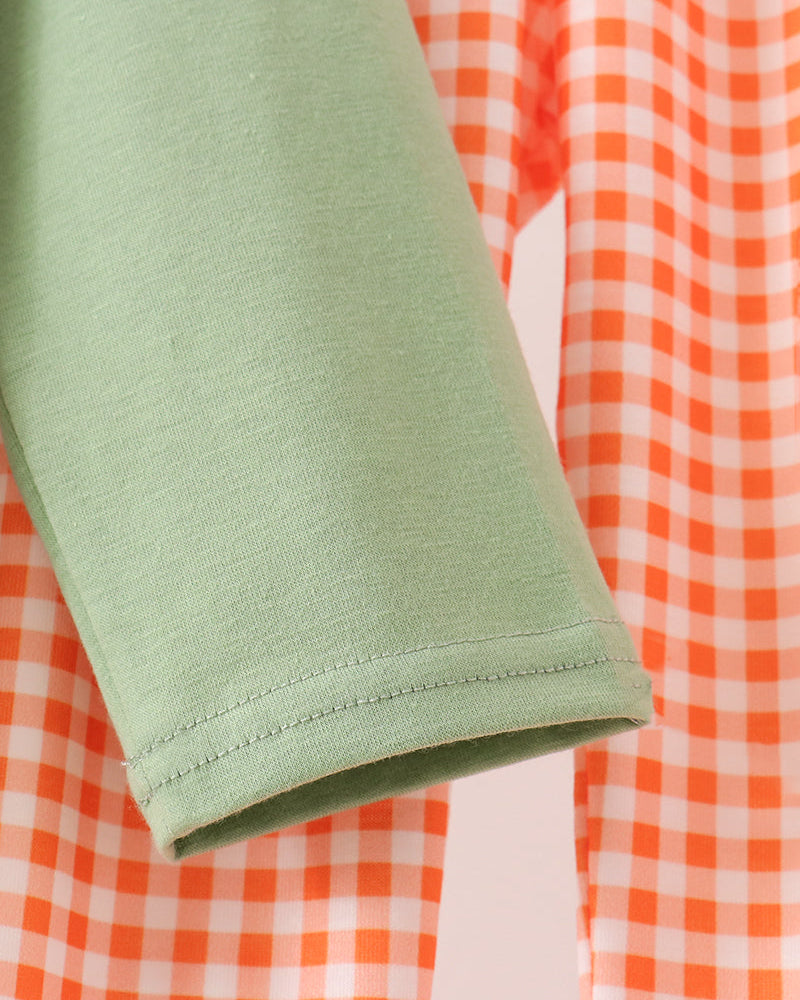 Close-up of a sage green sleeve with a neat hem, layered over an orange and white gingham patterned fabric.