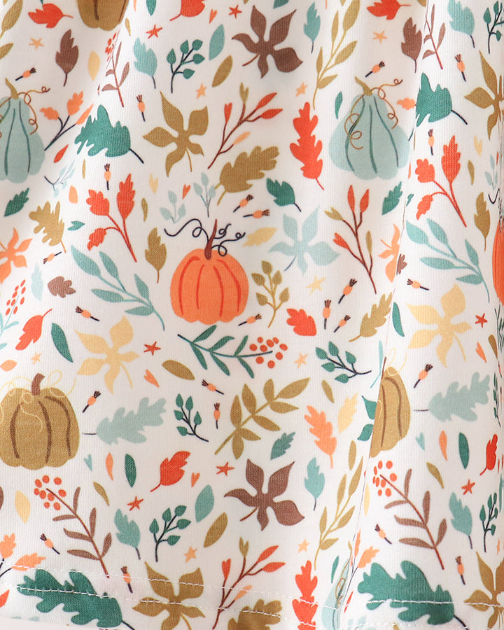 A close-up of a white fabric with an all-over autumn print featuring pumpkins, leaves, and branches in orange, teal, brown, and beige tones.
