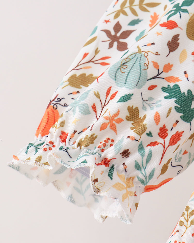 A close-up of a white fabric sleeve or garment cuff with a colorful autumn leaf and pumpkin print, finished with a ruffled hem.