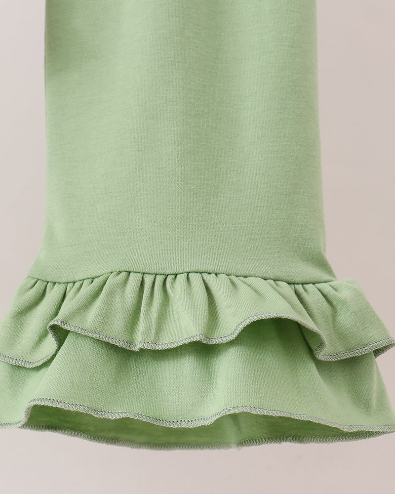 Close-up of a light sage green garment with a ruffled hem, showing the fabric texture and layered ruffle details against a plain light background.