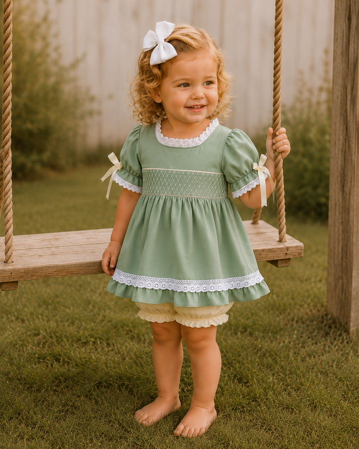 Child wearing sage green smocked lace dress with bow details and cream bloomers