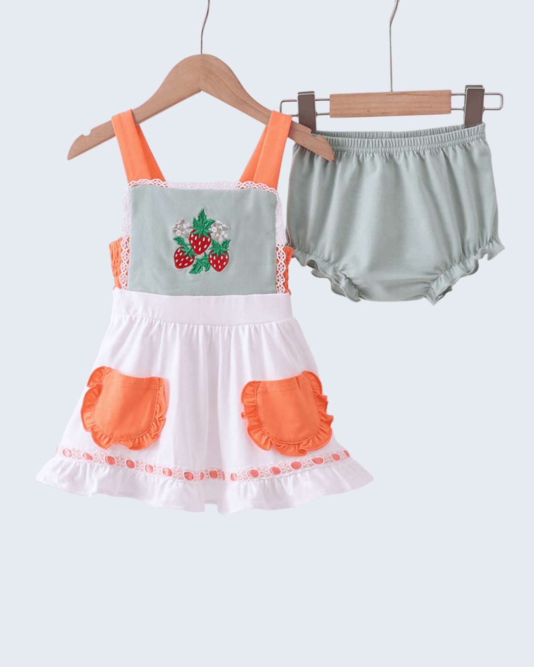 Children's dress with strawberry design and matching bloomers on hangers against a white background