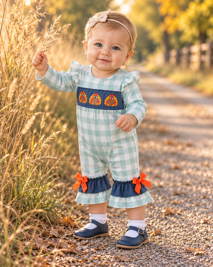 Baby girl is wearing a Sage Turkey Embroidered Gingham Ruffle Romper