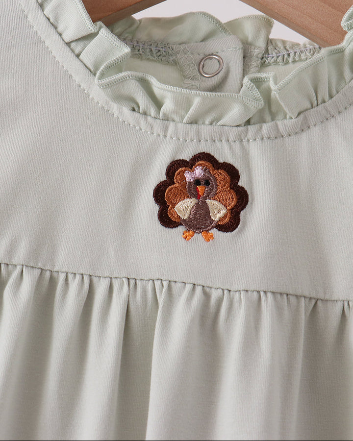 Close-up of ruffle neckline and turkey applique on light romper, button placket