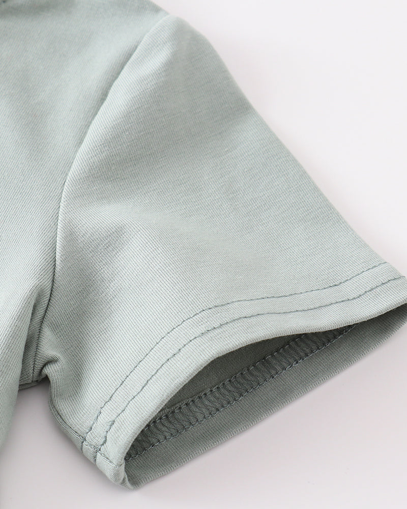 Close-up of a light sage green fabric garment, showing the texture of the woven material and a rolled cuff with neat stitching, on a plain white background.