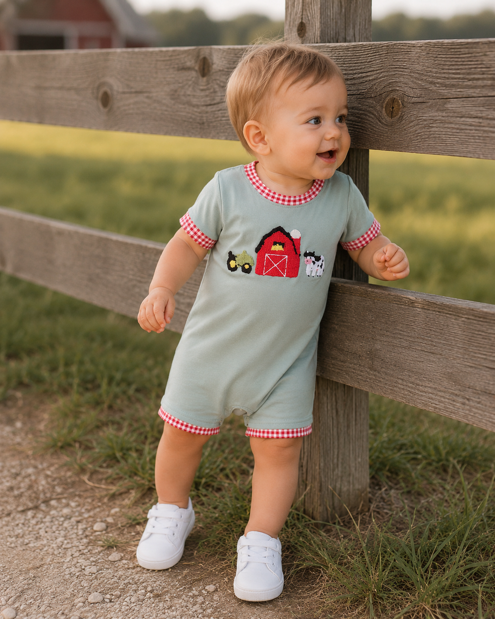 Baby boy is looking through a wooden fence onto a pasture.