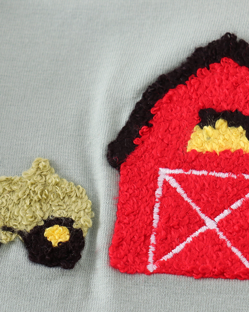 Close-up of a textured red barn applique with white trim and a yellow window detail, alongside a smaller beige and black applique, on a light gray fabric background.