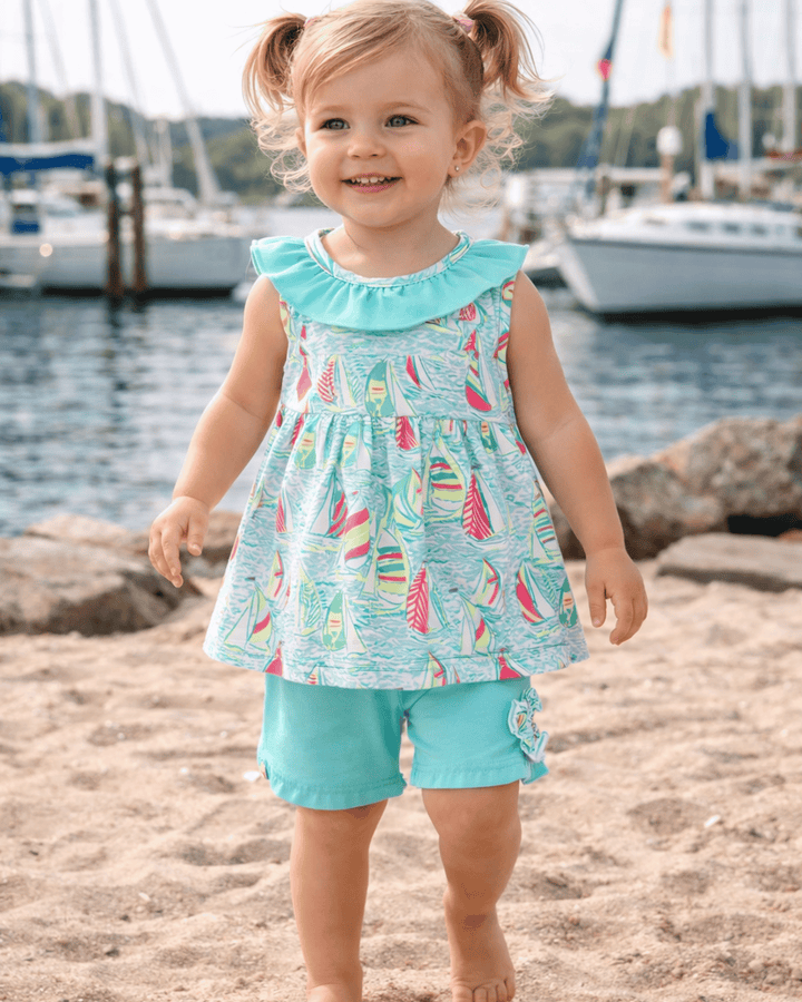 Child wearing a light blue dress with sailboat pattern by a marina.