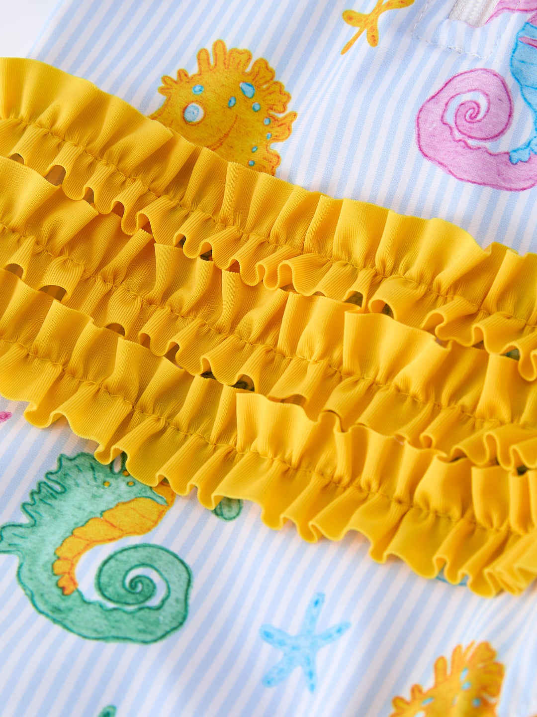 Yellow ruffled trim on a colorful fabric background with sea-themed designs.