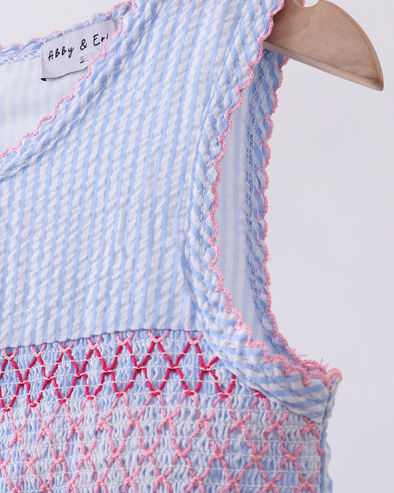 Close-up of a blue and white checkered dress with pink smocking detail on a white background.