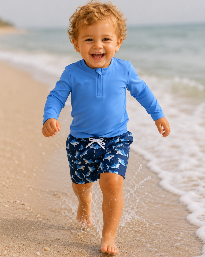 Child in blue shirt and shark-patterned shorts running on a beach