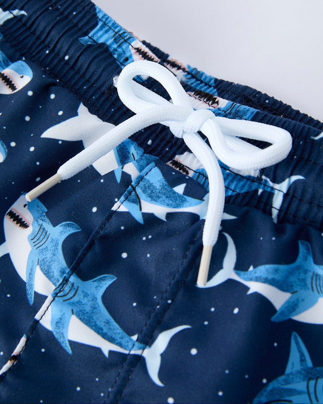 Navy swim shorts with shark pattern and white drawstring on a light gray background