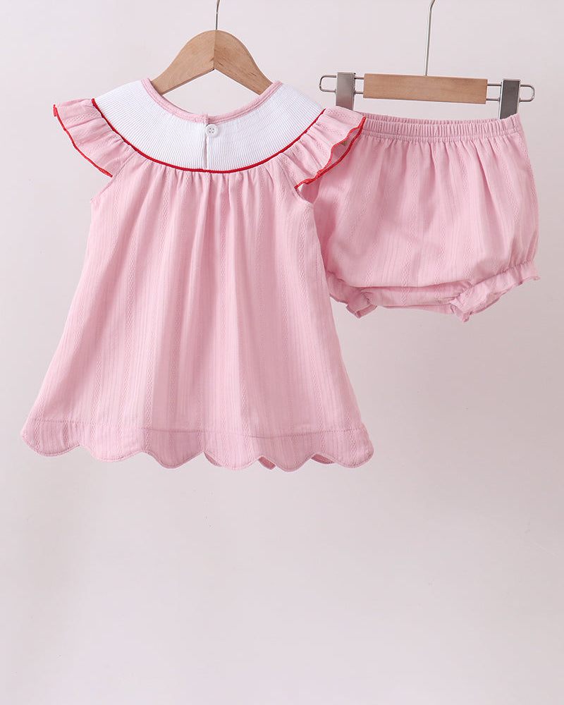 Pink baby outfit with ruffled top and bloomers on hangers against a light pink background