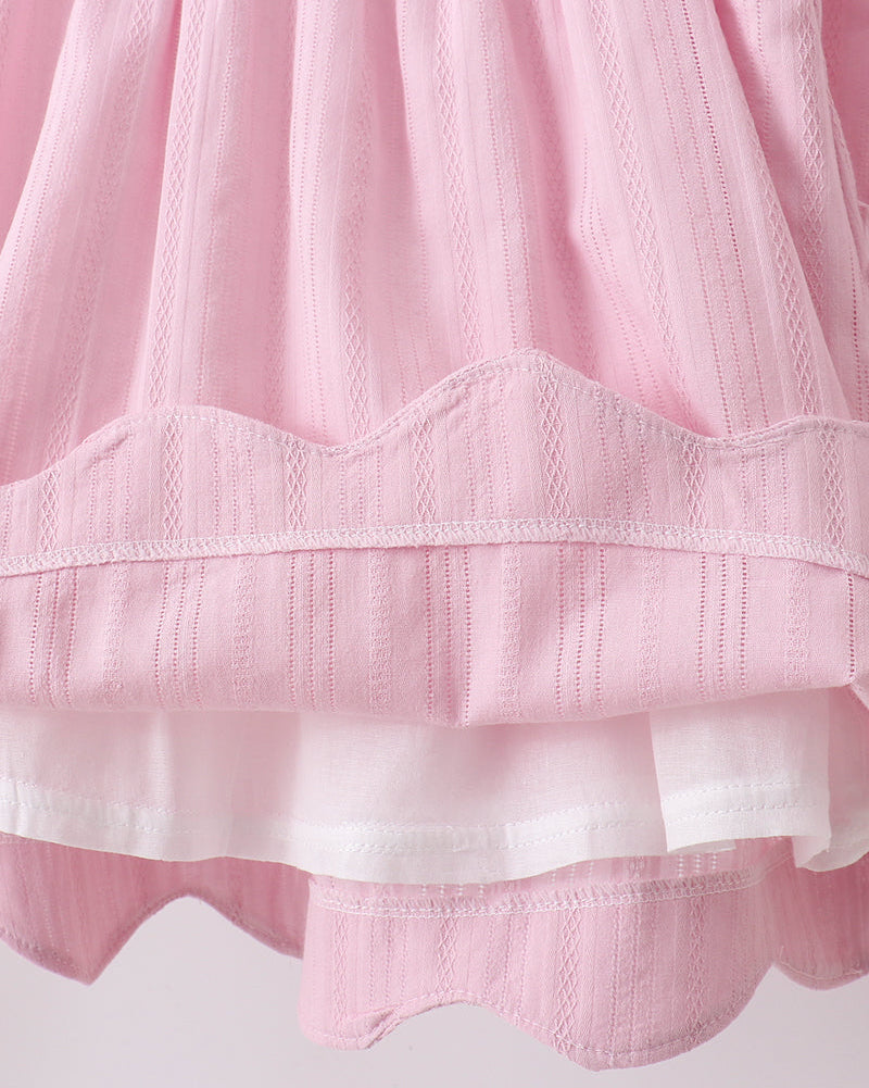 Close-up of a pink and white textured fabric with scalloped edges on a light background