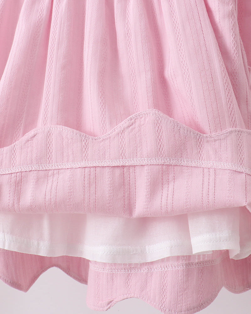 Close-up of a pink and white textured fabric with scalloped edges on a light background