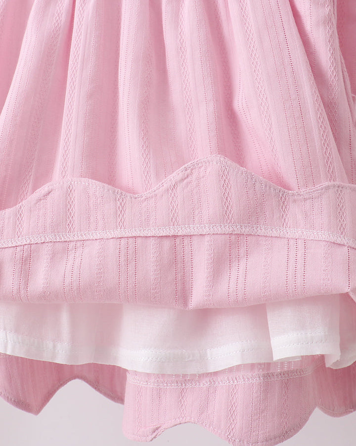 Close-up of a pink and white textured fabric with scalloped edges on a light background