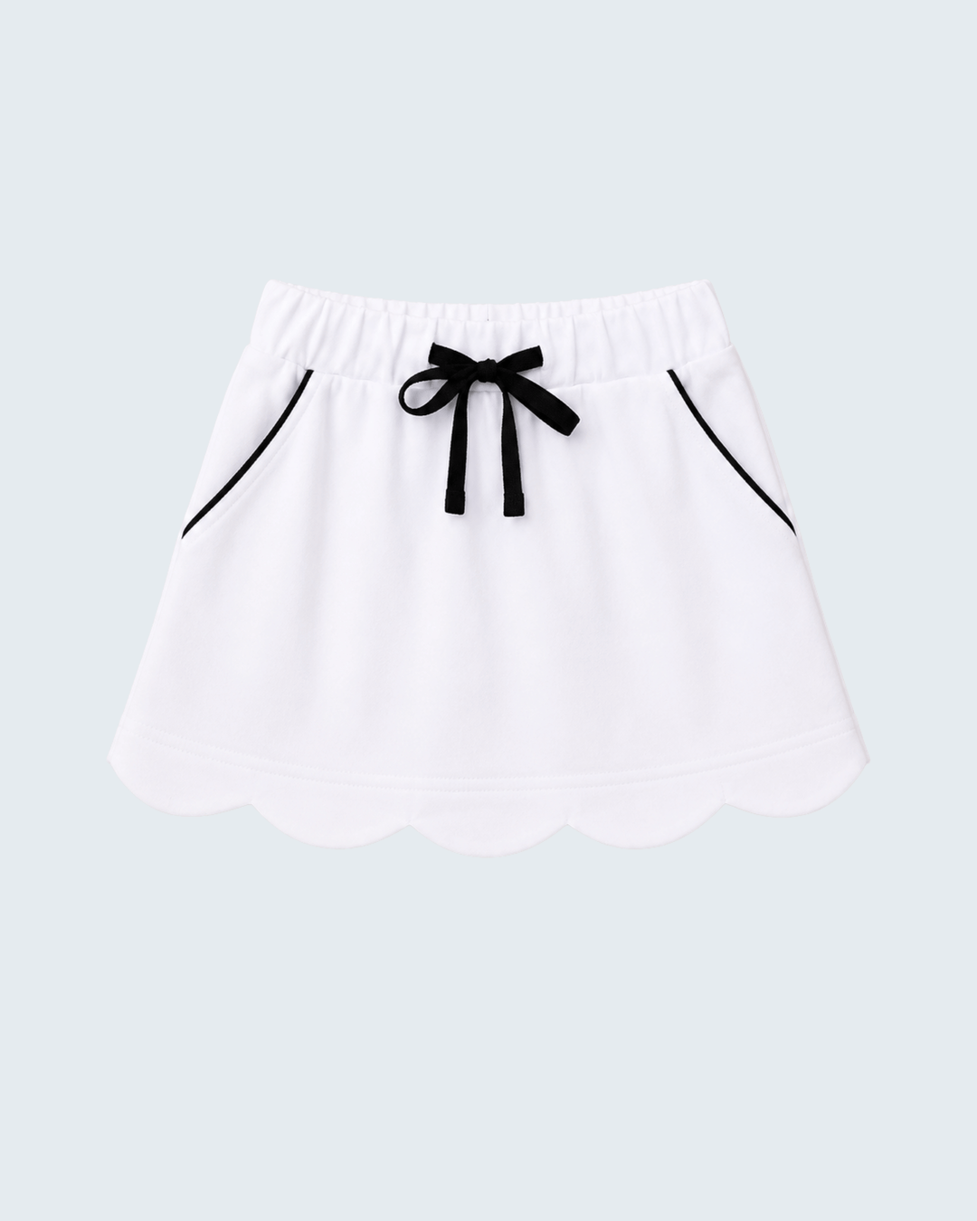 A white skort with a scalloped hem, an elastic waistband, a black ribbon bow at the center, and thin black piping details on the sides, shown against a light gray background.