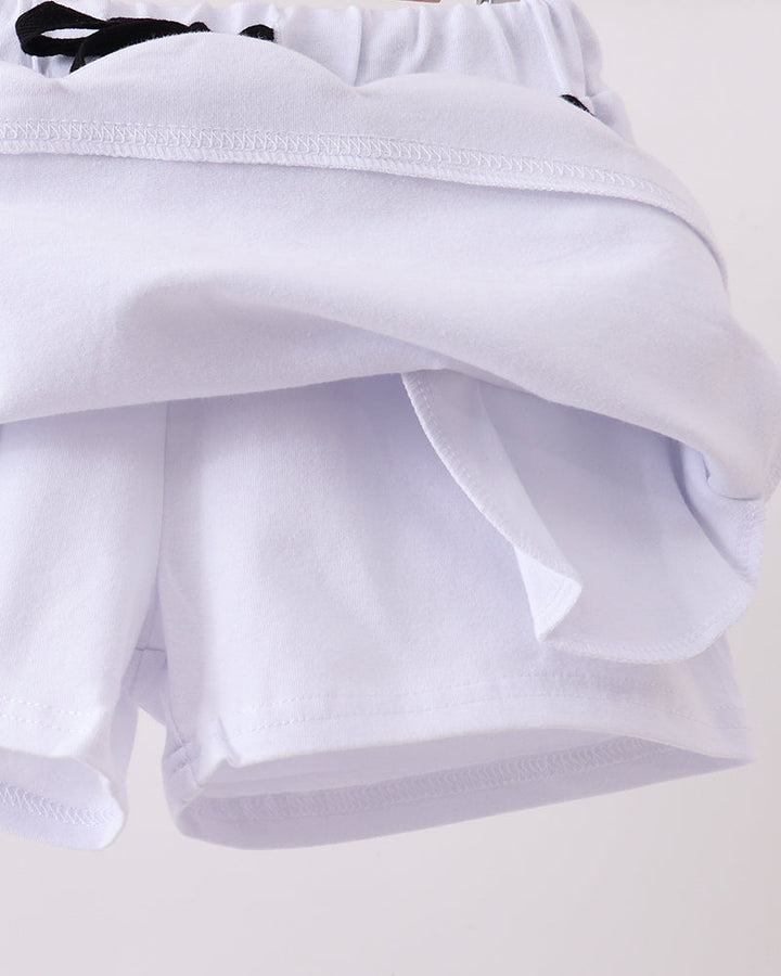 White scallop-hem skort with layered ruffle panel and black bow tie ends