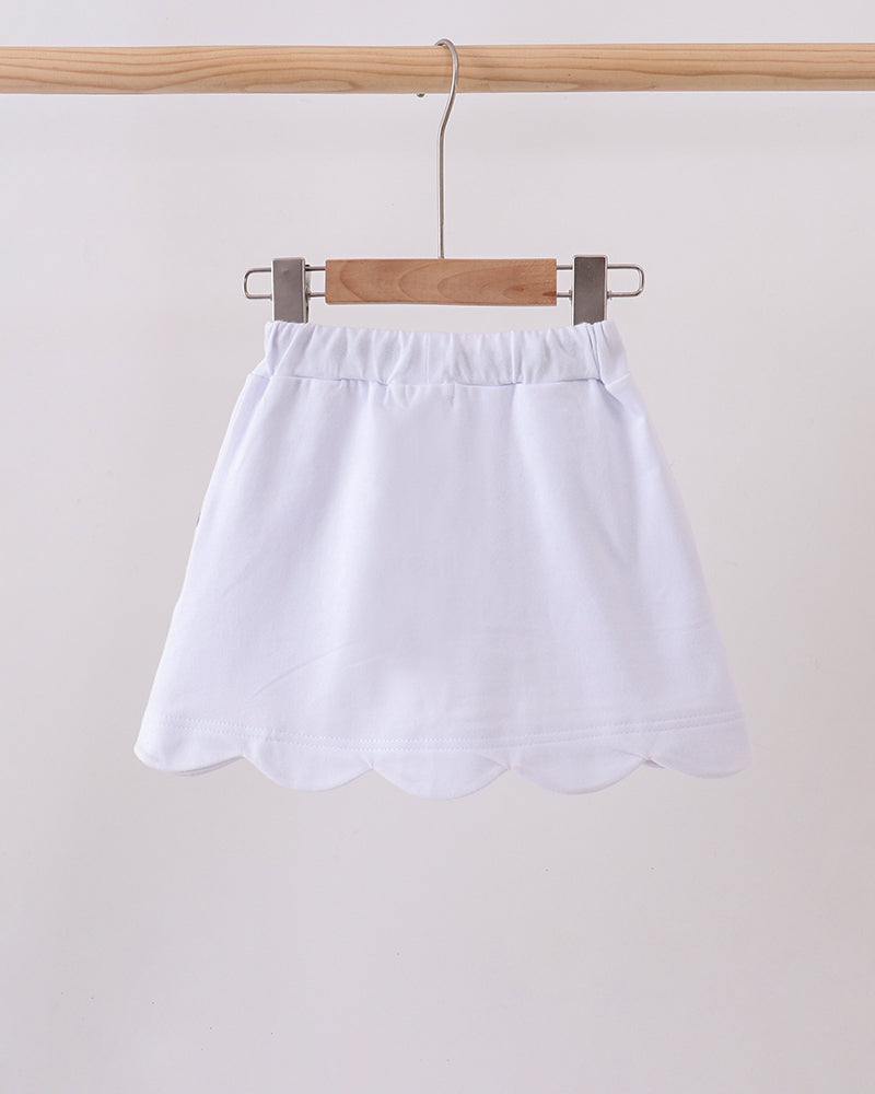 White scalloped hem skort on hanger with elastic waist and black bow