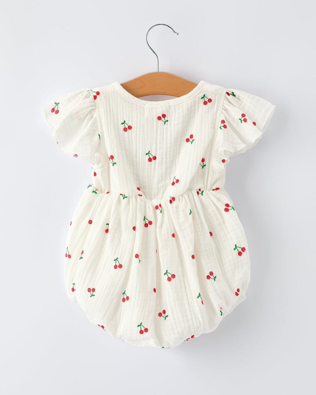 White baby romper with red cherry pattern on a white background