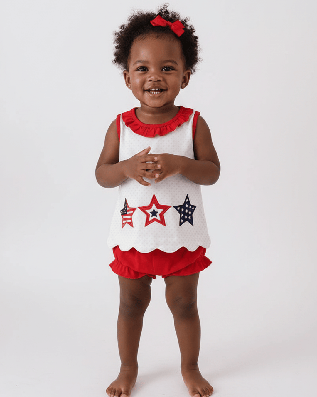 Child wearing a white sleeveless top with red and blue star designs and red ruffled shorts on a white background.