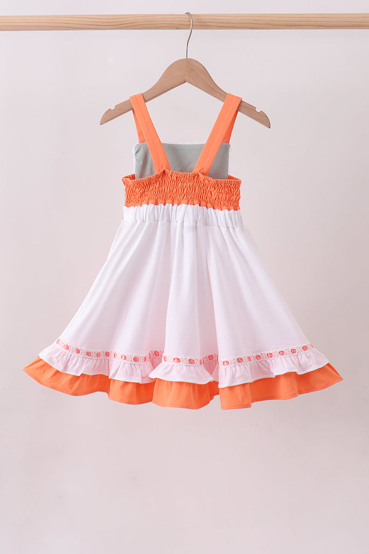 White dress with orange trim on a hanger against a plain background