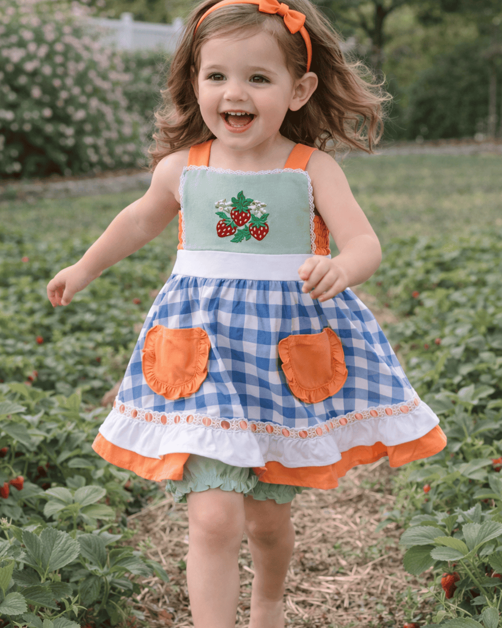 Child wearing a blue and orange dress with strawberry design in a strawberry field