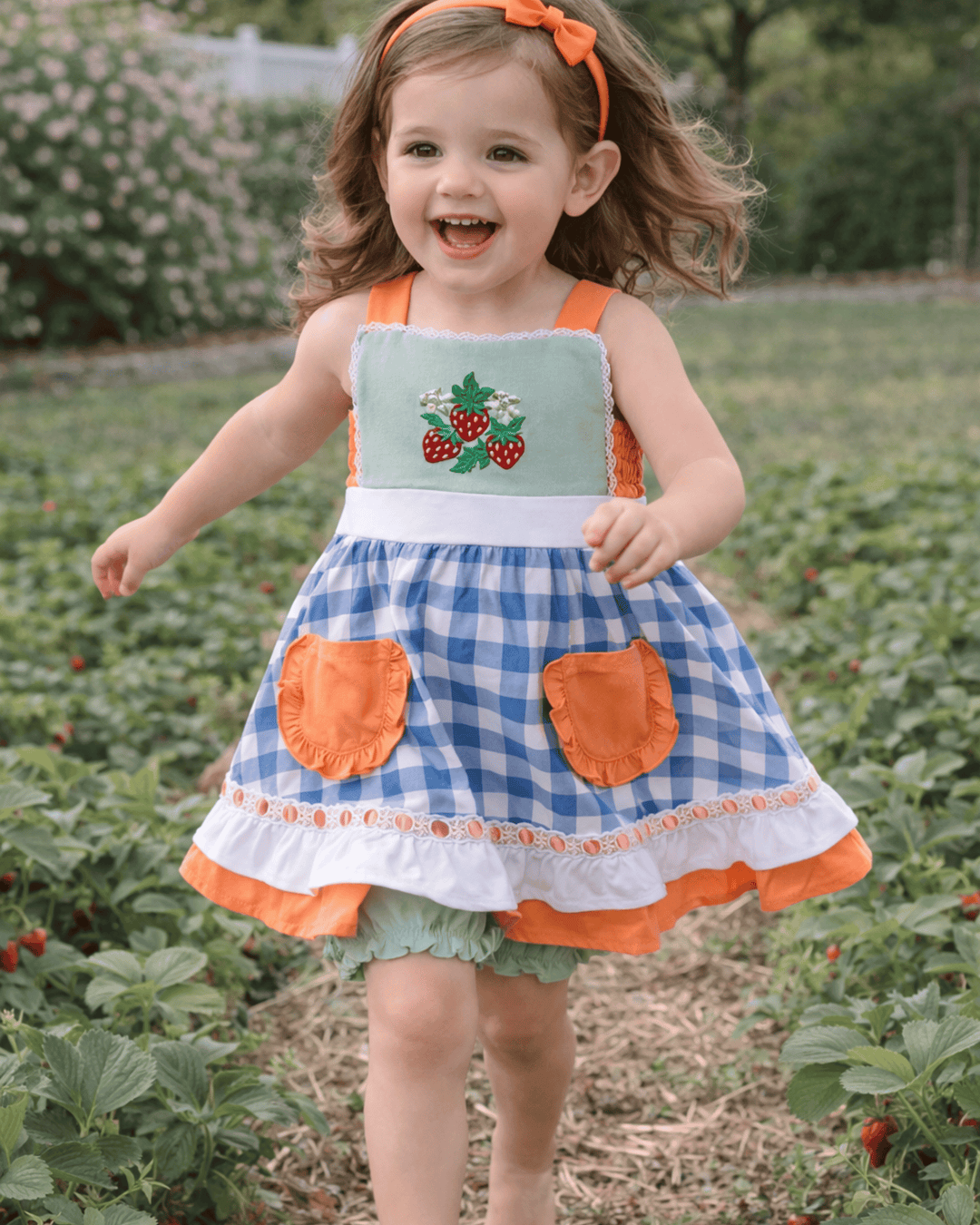 Child wearing a blue and orange dress with strawberry design in a strawberry field