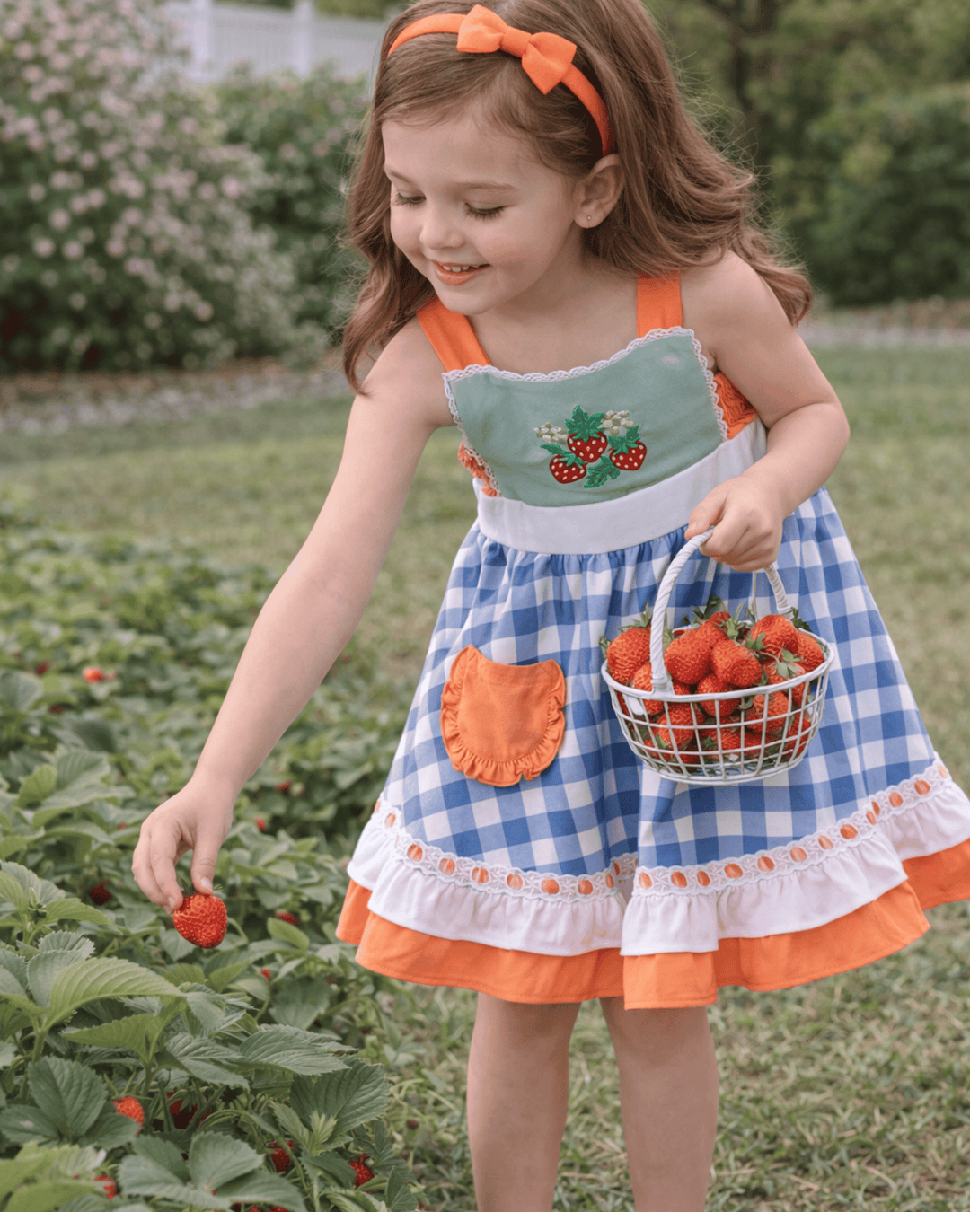 Young girl in a checkered dress with an apron holding a basket of strawberries in a strawberry field.